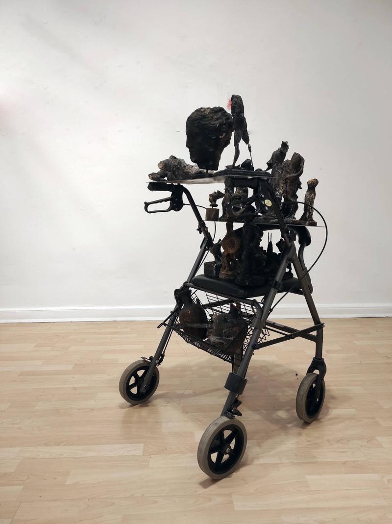 Image depicting the artwork named Βασίλης Αλεξάνδρου - "Turismo", 2025, τροχήλατος περιπατητήρας, σίδερο, αποκαΐδια, 150x50x60cm.